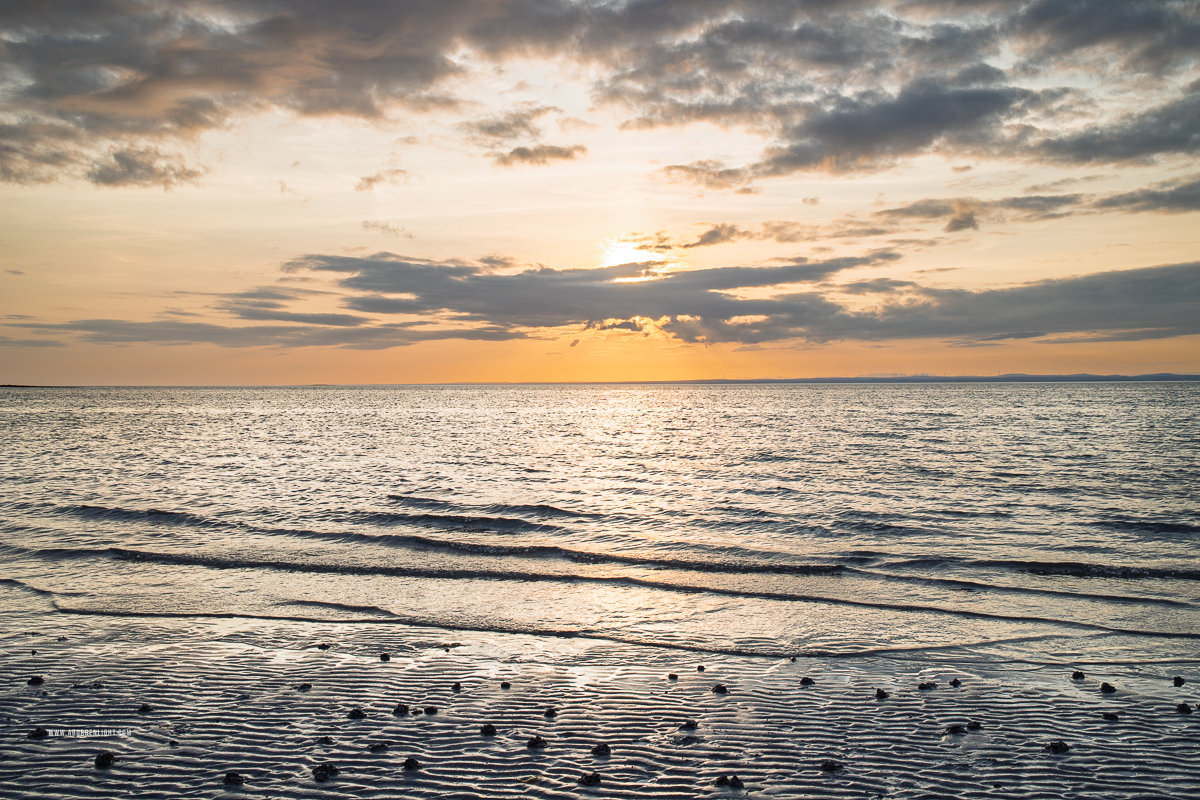 Golden sunset above gentle waves, scattered pebbles and rippled wet sand at Traught Beach near Kinvara.