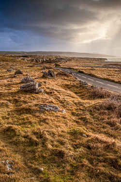 A narrow track crossing golden winter grass and exposed limestone beneath dramatic storm clouds near Fanore