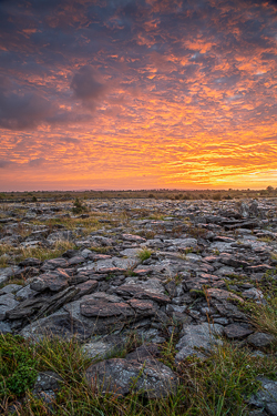Orange dawn spreading above an open expanse of fractured limestone pavement in the Burren
