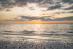 Golden sunset above gentle waves, scattered pebbles and rippled wet sand at Traught Beach near Kinvara.